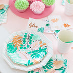 Table setting with floral-patterned plates, Aqua green striped paper napkins, and a cup on a pink surface.