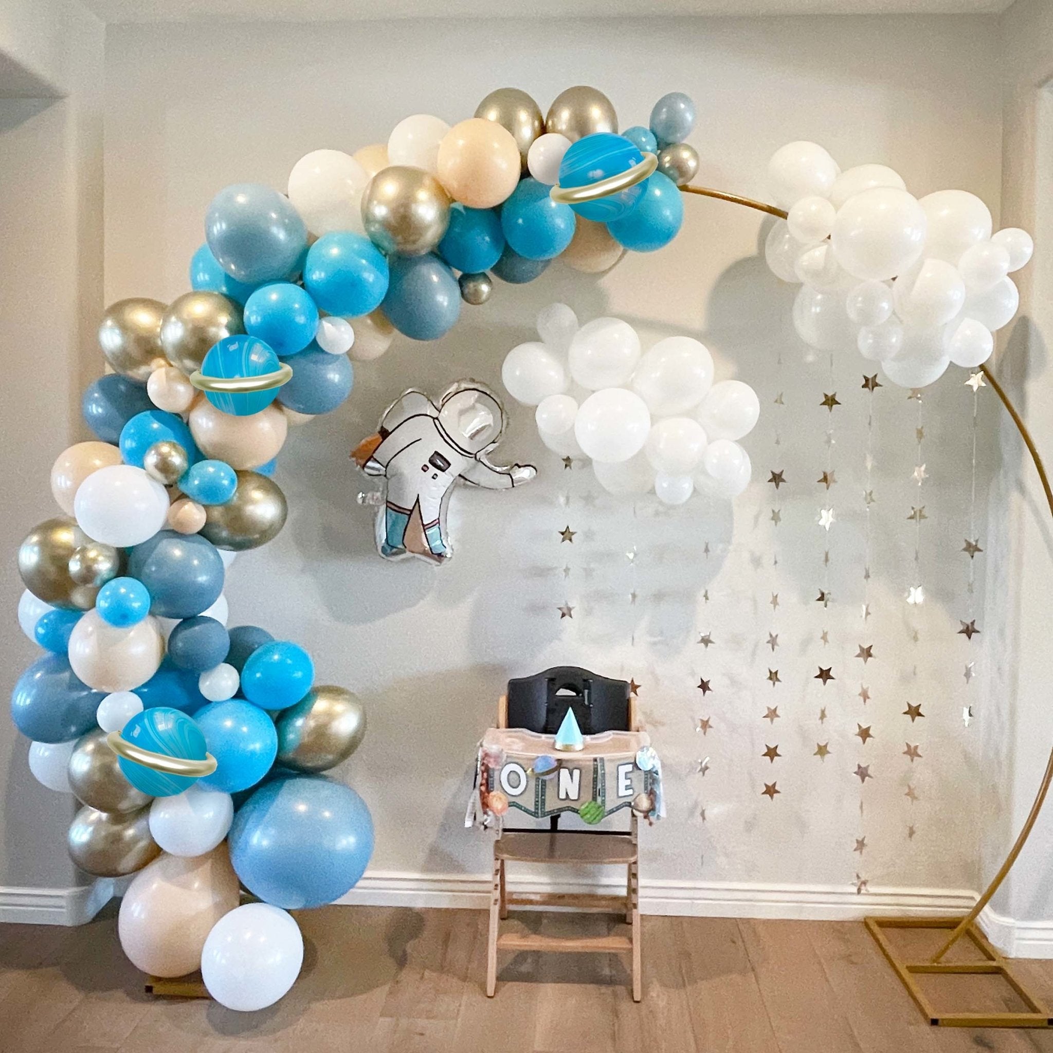 Balloon arch with blue, gold, and white balloons in a room with a star-patterned curtain. Main image