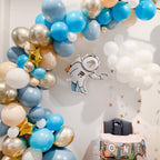 Balloon arch with blue, gold, and white balloons and an astronaut balloon in a room.