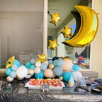 Decorative setup with balloons and food on a table, featuring gold stars and a moon shape.