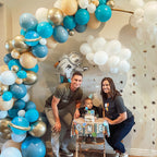 Family celebrating a child's first birthday with a balloon arch and 'ONE' banner.