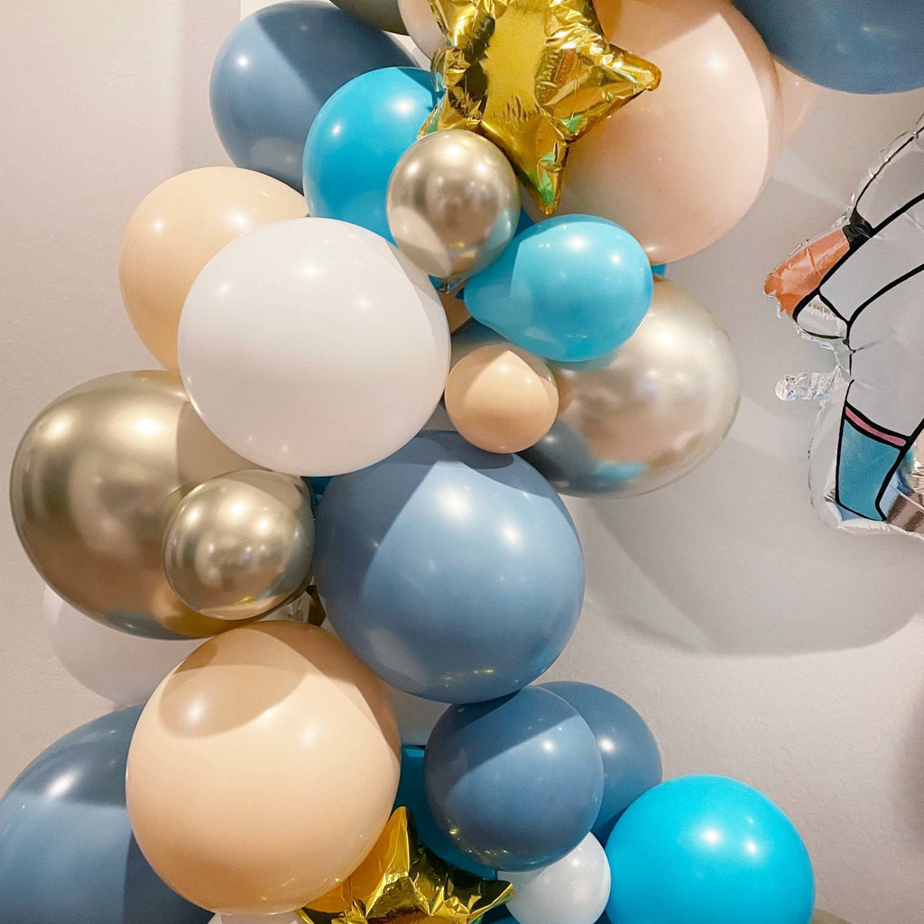 Colorful balloon arch with blue, gold, beige, and white balloons against a light background.