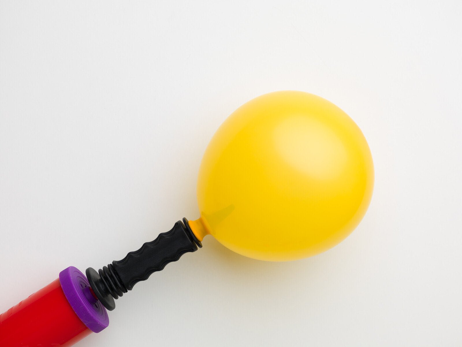 Yellow balloon being inflated with a red and purple pump on a white background