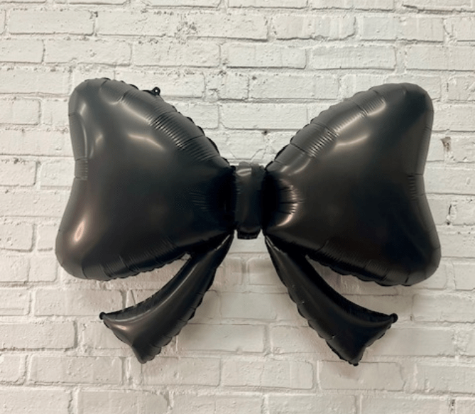 Black bow-shaped balloon against a white brick wall background