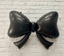 Black bow-shaped balloon against a white brick wall background