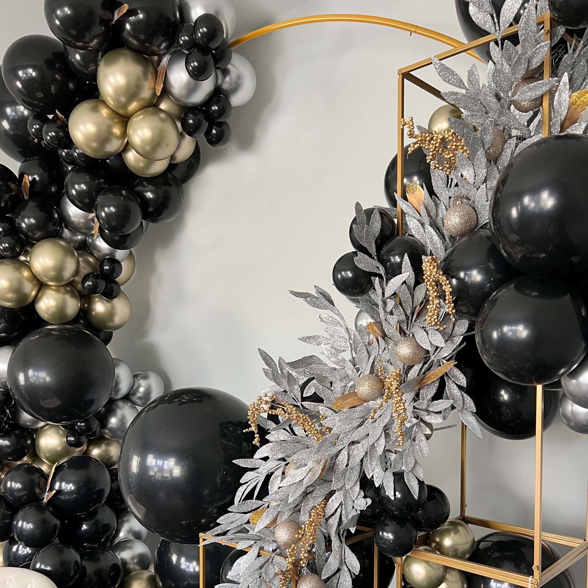 Decorative wreath with black, gold, and silver balloons against a neutral background