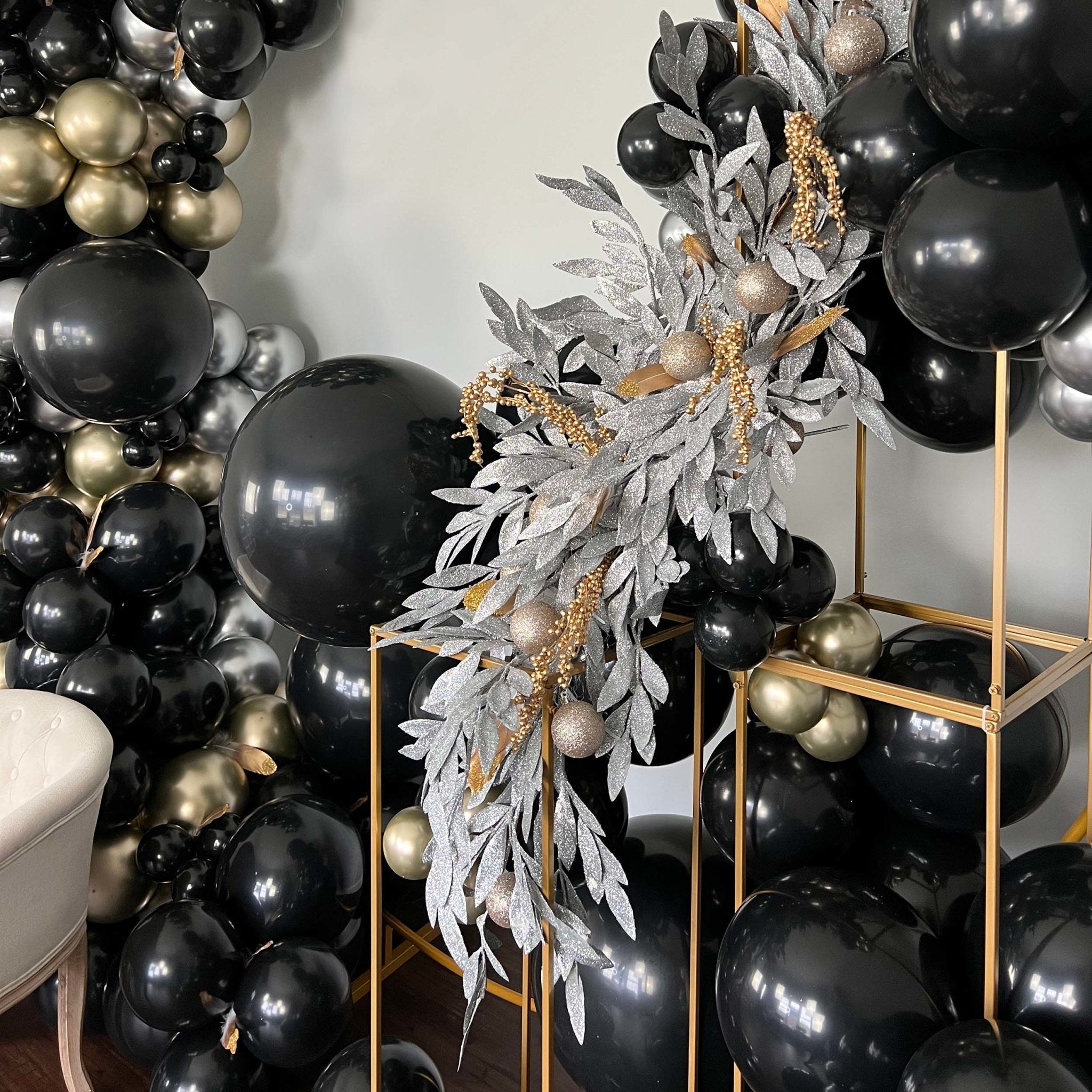 Decorative wreath with black, gold, and silver balloons and foliage on a stand.