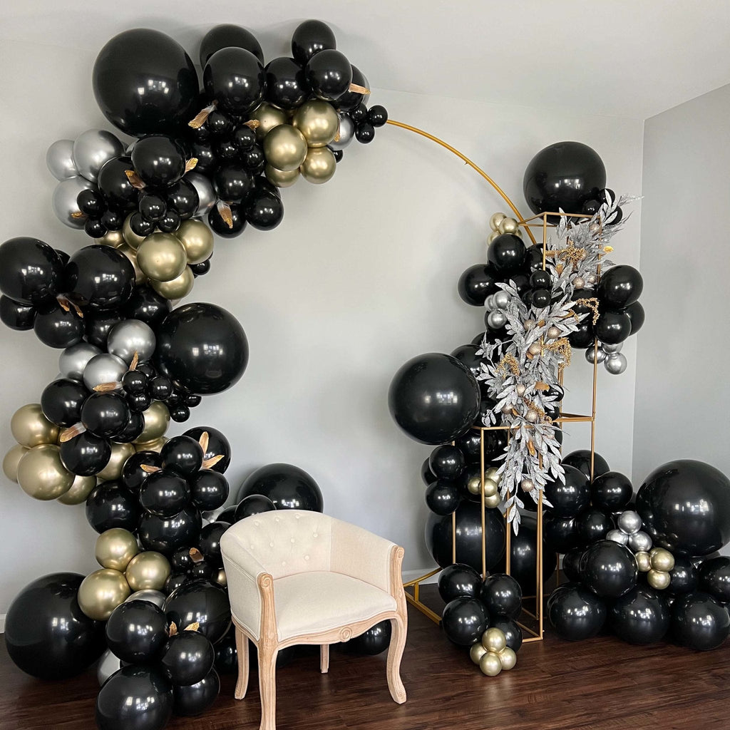 Balloon arch with black, gold, and silver balloons in a room with a chair.