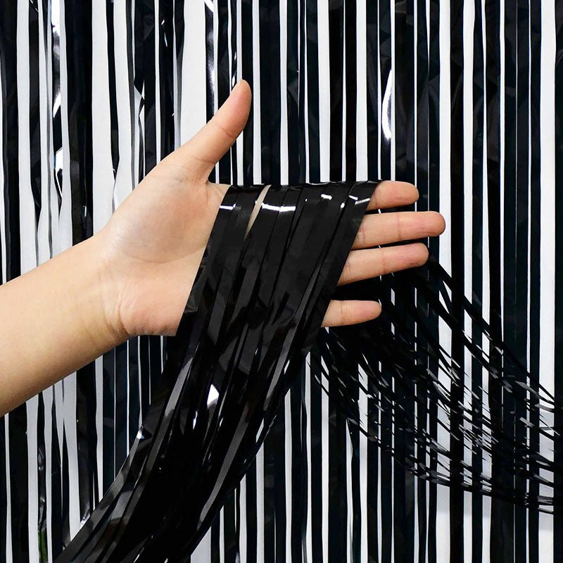 Hand holding black tinsel against a black and white striped background Main image