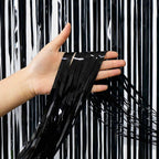 Hand holding black tinsel against a black and white striped background
