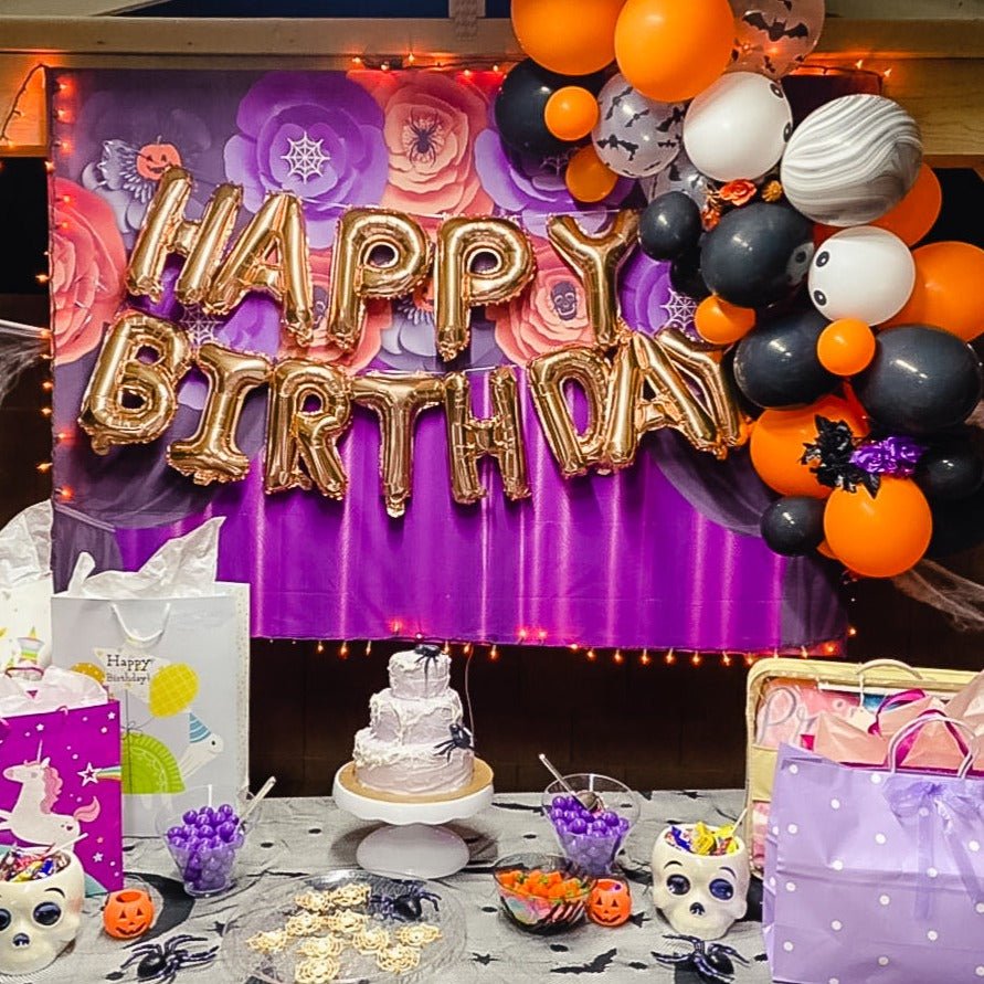 Halloween-themed birthday party setup with balloons, cake, and decorations.