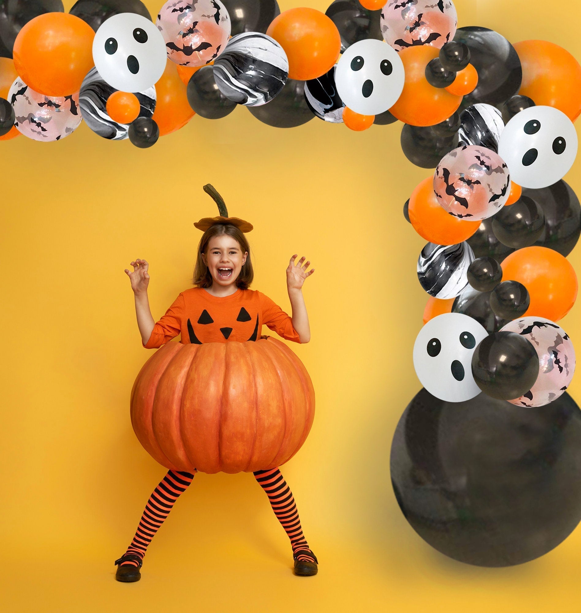 Child in a pumpkin costume with Halloween-themed balloons on a yellow background