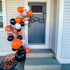 Halloween-themed balloon arch on a front porch with candy basket.