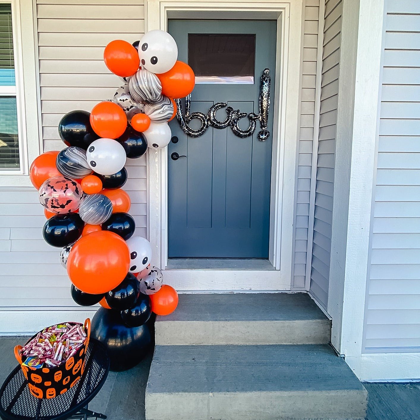 Halloween-themed balloon arch on a front porch with candy basket.