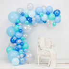 Balloon arch with blue, green, and white balloons against a white wall.