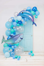 Decorative balloon arch with dolphin and shark balloons against a light blue door.