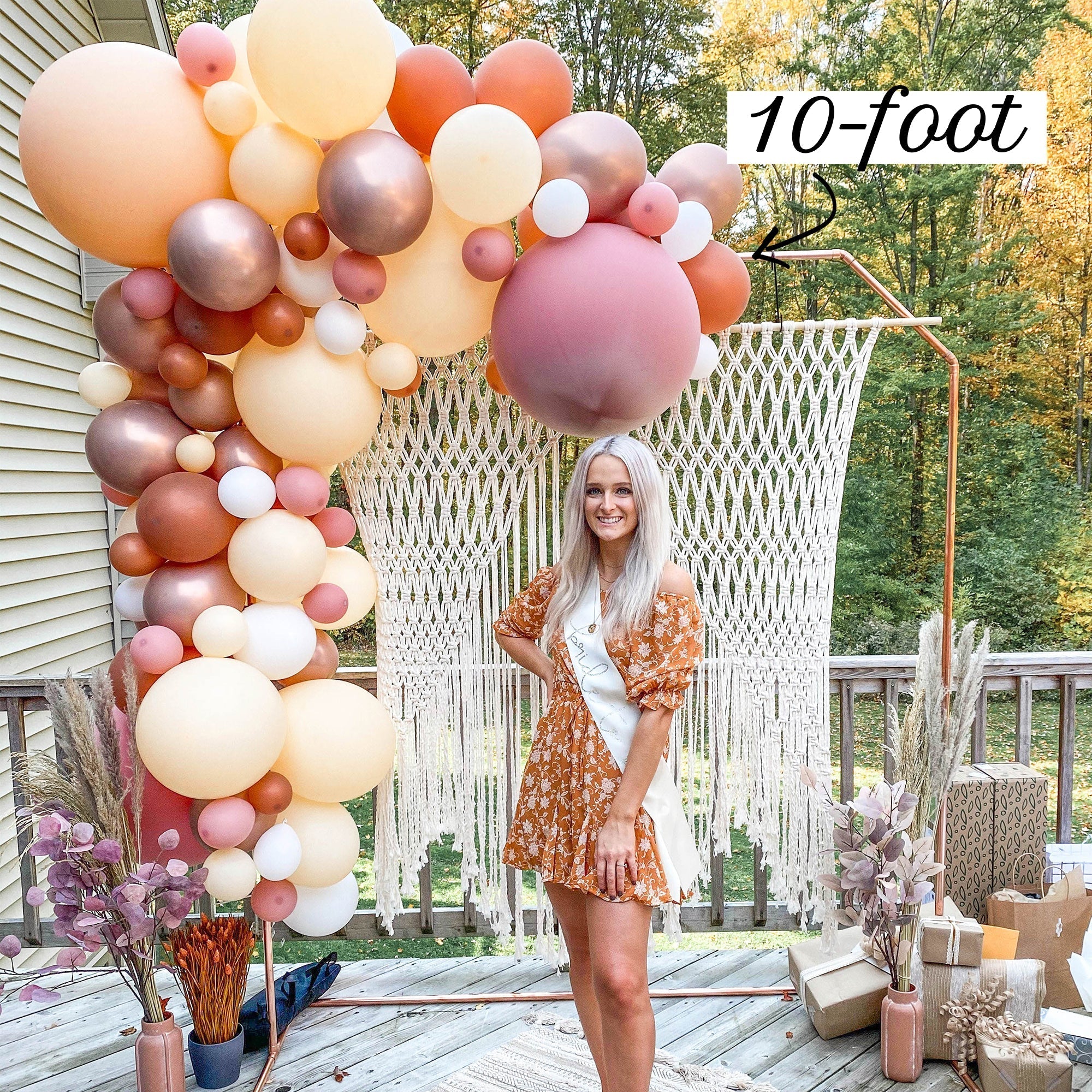 Woman standing next to a large balloon arch on a deck with decorative plants and furniture.