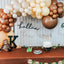 Decorative setup with balloons, sloth toys, and a cake on a table against a wooden wall.