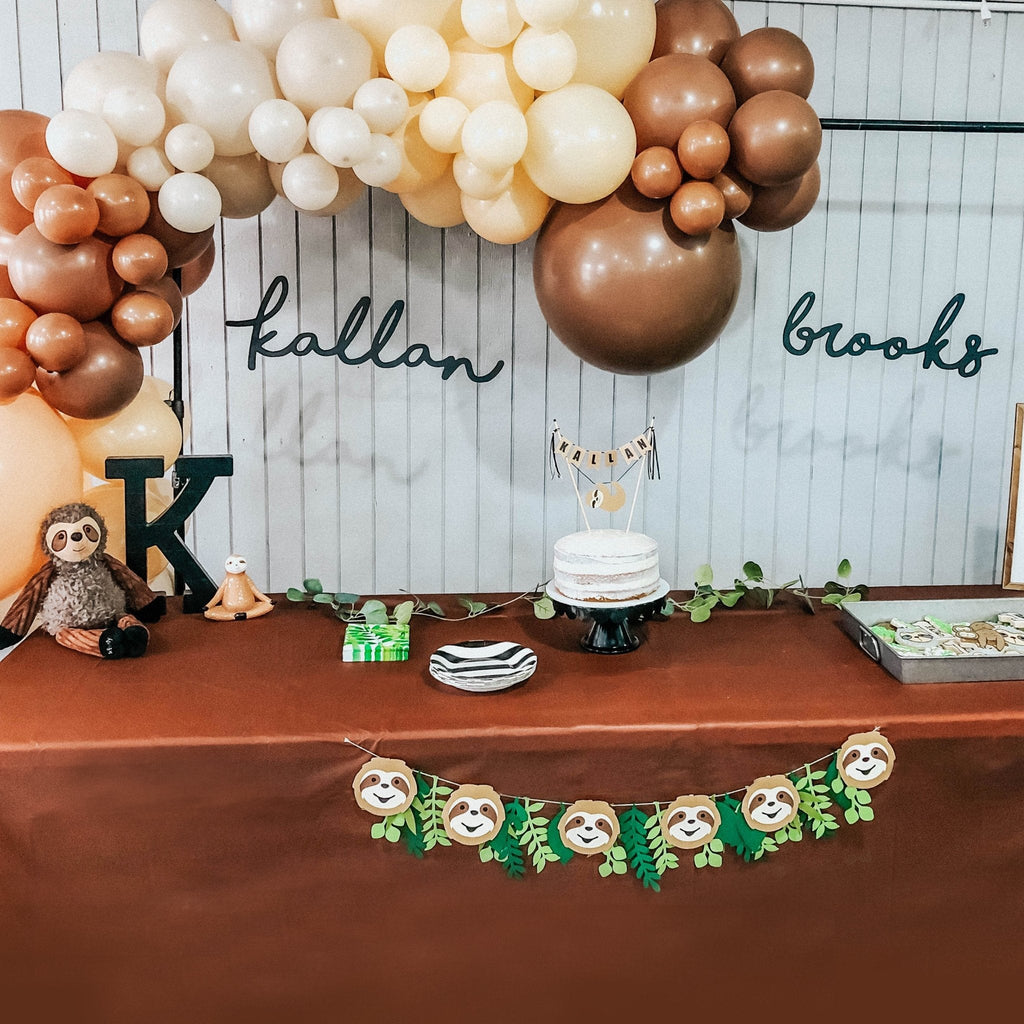 Decorative setup with balloons, cake, and sloth-themed decorations on a table.