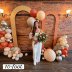 Woman standing in front of a decorative arch with balloons and flowers, against a brick wall.