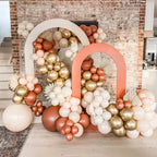 Decorative balloon Garland with pink, gold, and white balloons against a brick wall.