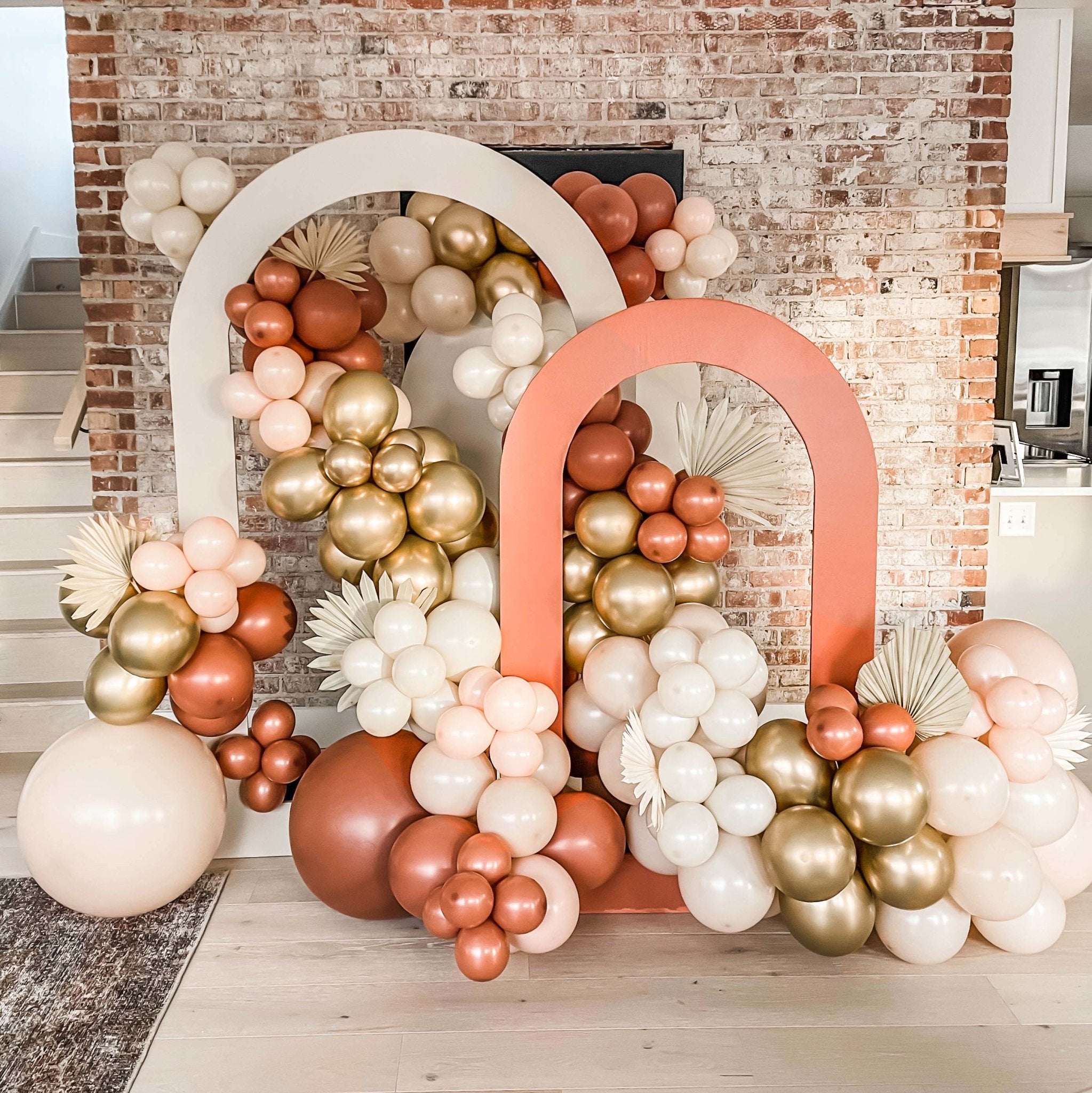 Decorative balloon Garland with pink, gold, and white balloons against a brick wall.