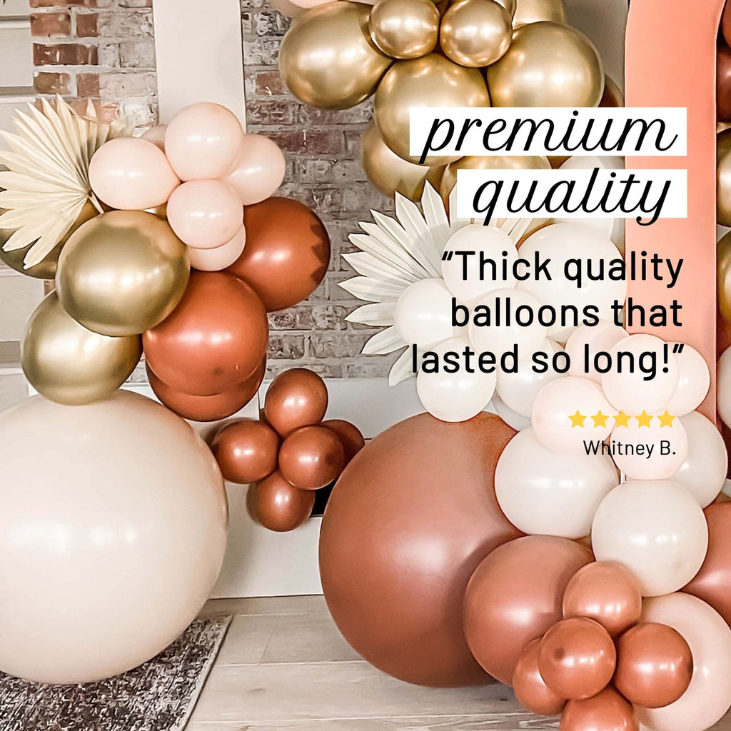 Decorative balloon arch with gold, white, and brown balloons against a brick wall.