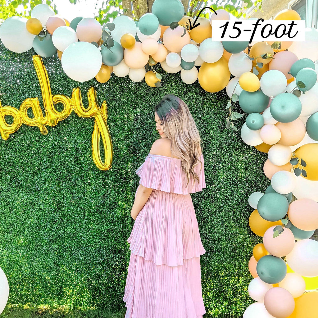 Woman in a pink dress standing under a large balloon arch with 'baby' balloons and a 15-foot label.