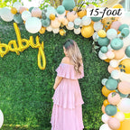 Woman in a pink dress standing under a large balloon arch with 'baby' balloons and a 15-foot label.