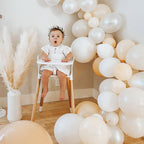 Baby in a high chair surrounded by white and beige balloons in a room with Balloon Garland.