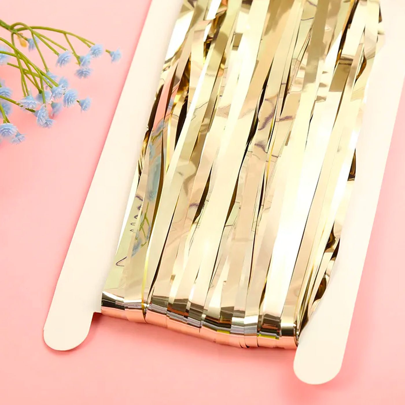Champagne gold metallic fringe tinsel curtain backdrop on a pink background with small blue flowers