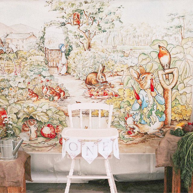 Decorative peter rabbit backdrop mural with animated rabbits and garden scene, featuring a chair with 'ONE' banner.