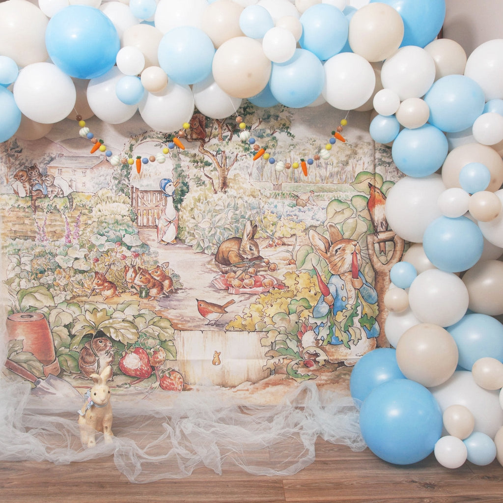Balloon arch with blue and white balloons in front of a Peter Rabbit Photo illustration Backdrop