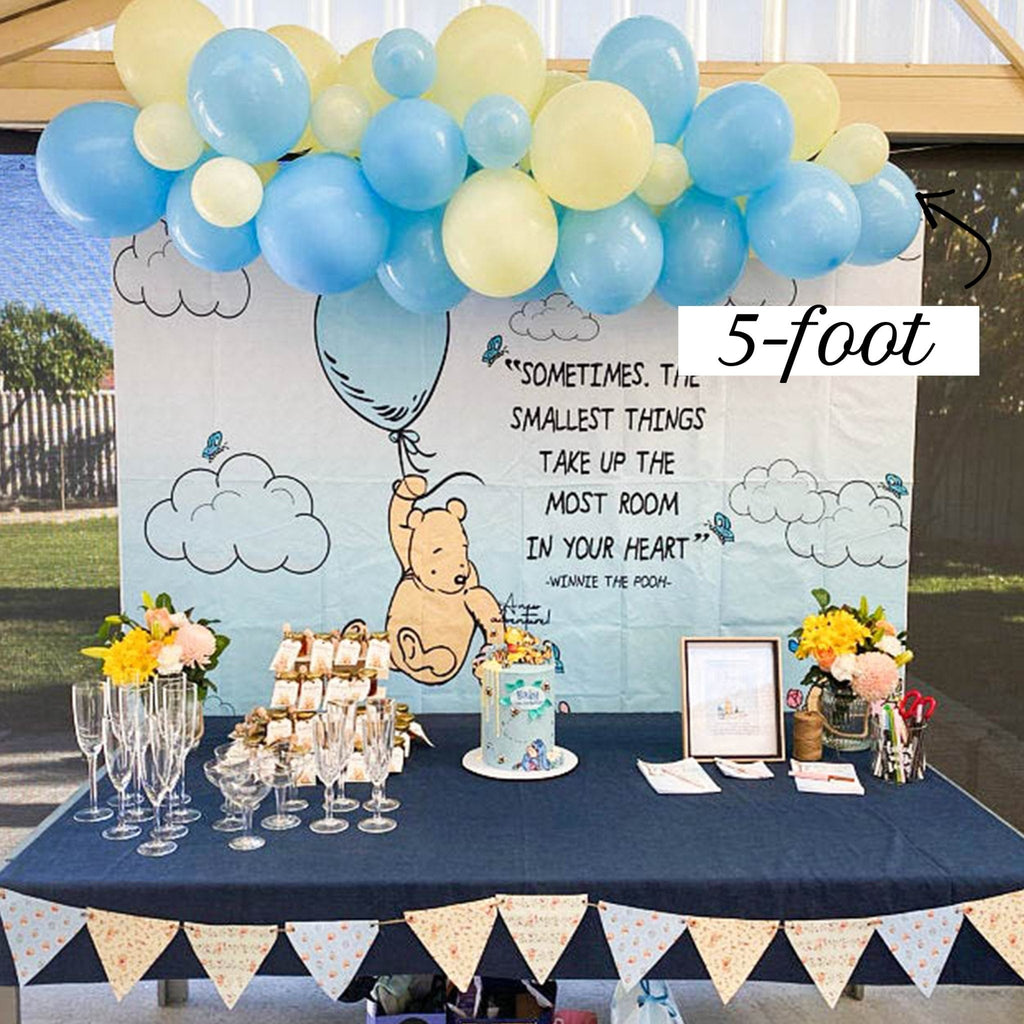 Decorated table with balloons, flowers, and a Winnie the Pooh-themed backdrop.