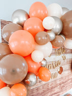 Balloon arch with orange, beige, and silver balloons on a wooden surface.