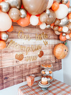 Decorative balloon arch with 'Our little pumpkin is one' sign against a wooden wall.
