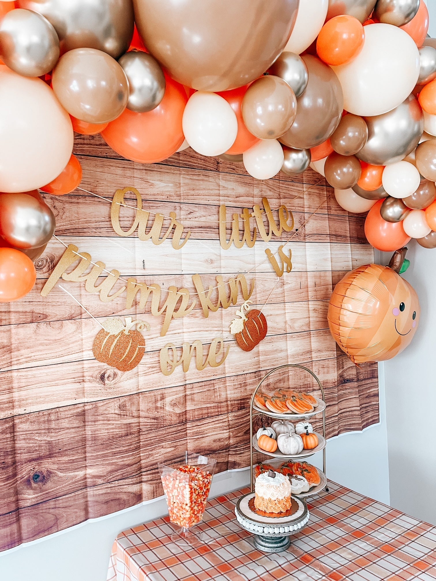 Decorative balloon arch with 'Our little pumpkin is one' sign against a wooden wall.