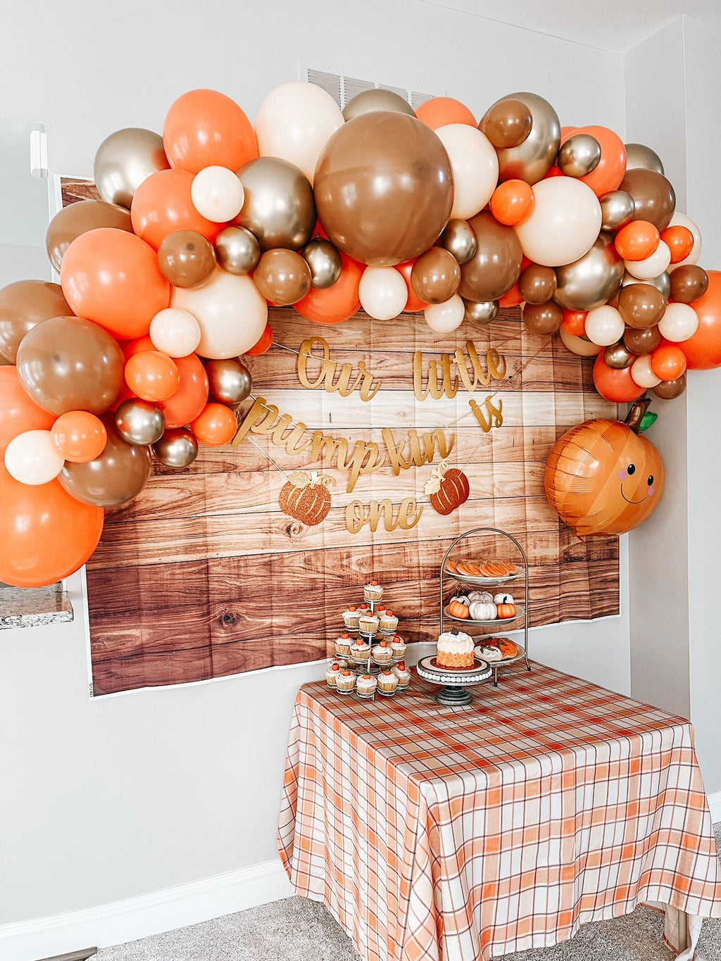 Decorative balloon arch with orange, brown, and white balloons above a table set for a celebration.