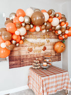 Decorative balloon arch with orange, brown, and white balloons above a table set for a celebration.