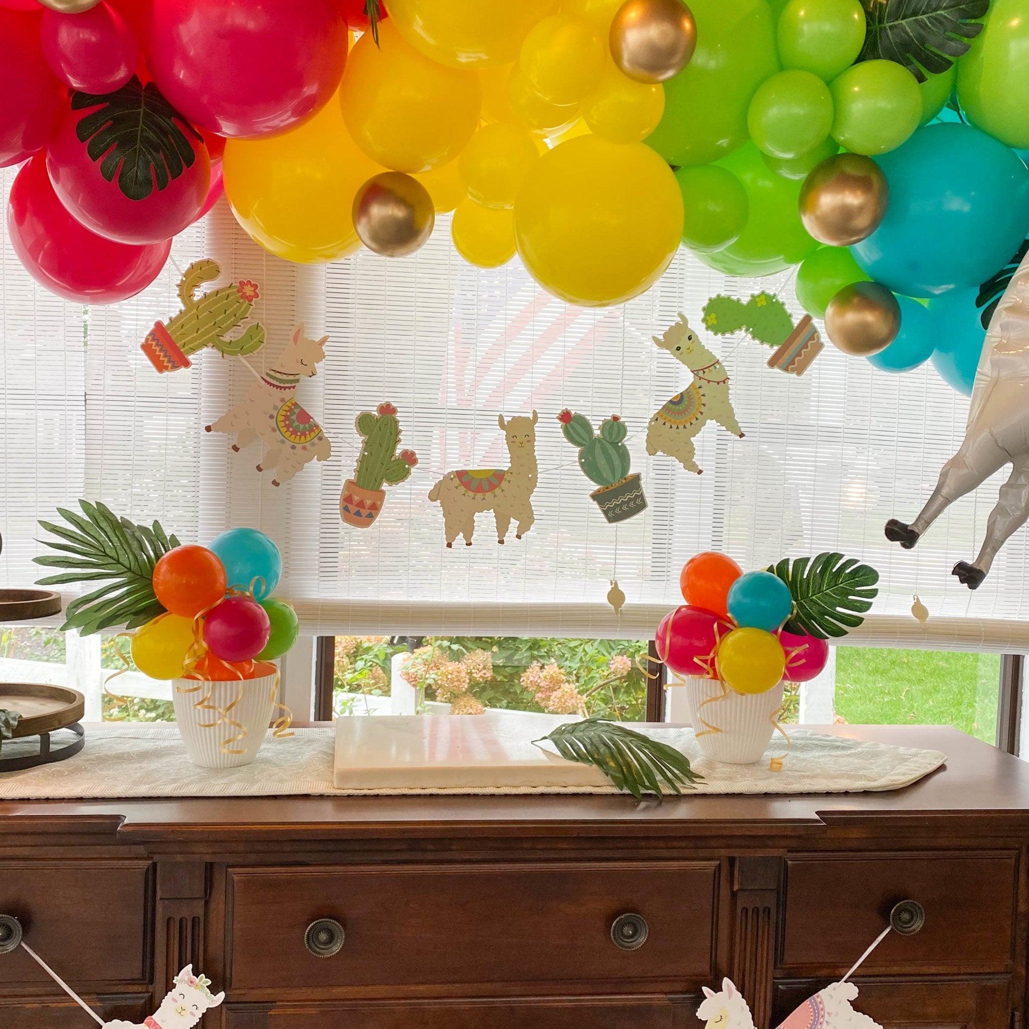 Decorative setup with colorful balloons, plants, and animal-themed decorations on a window.