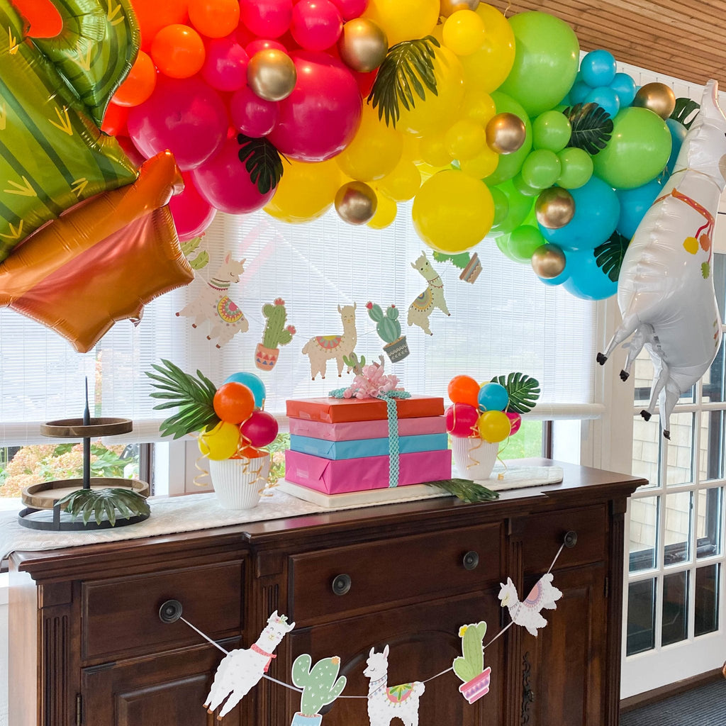 Decorative setup with balloons, gifts, and a llama-themed banner on a wooden cabinet.