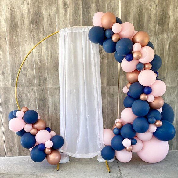 Balloon arch with pink, blue, and gold balloons against a wooden wall.