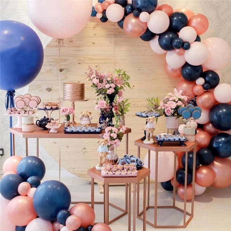 Decorative balloon arch with pink, blue, and white balloons at a party setup with tables and flowers.