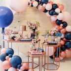 Decorative balloon arch with pink, blue, and white balloons at a party setup with tables and flowers.