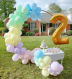 Outdoor birthday celebration with a balloon arch, cake, and number two balloon in front of a house.