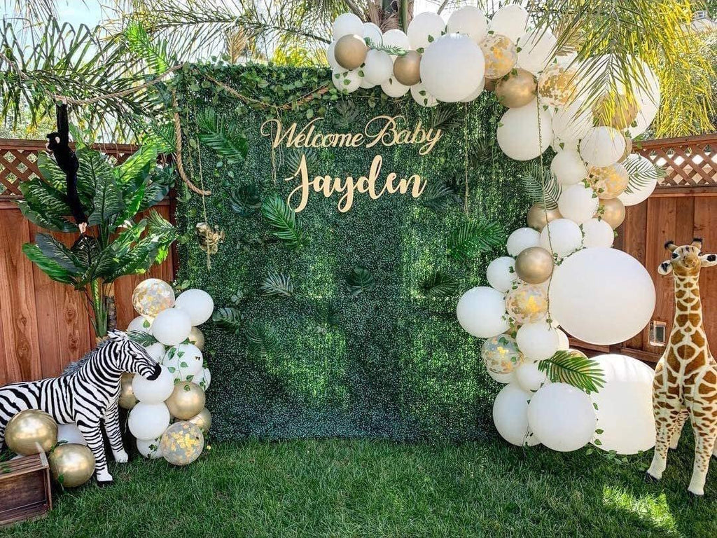 Decorative setup with balloons, a zebra figurine, and a 'Welcome Baby Jayden' sign in a garden.