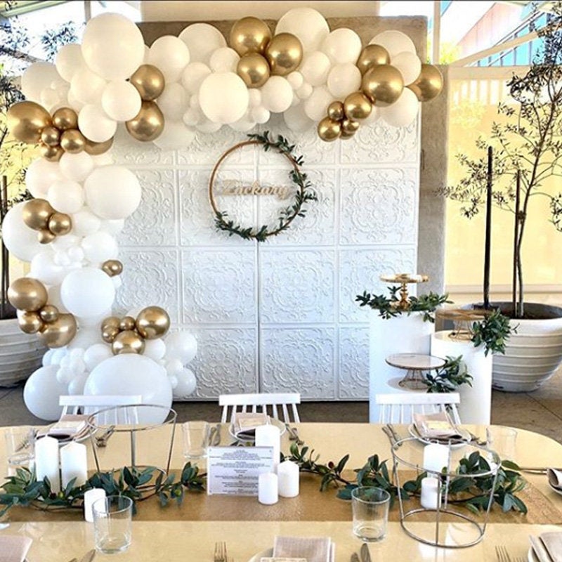 Decorative setup with balloons, table settings, and a wreath on a textured wall.