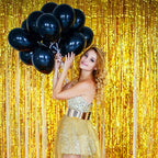 Woman holding black balloons against a Gold metallic fringe tinsel curtain backdrop 