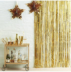 Decorative gold star decorations on a white brick wall with a Gold metallic fringe tinsel curtain backdrop and bar cart.