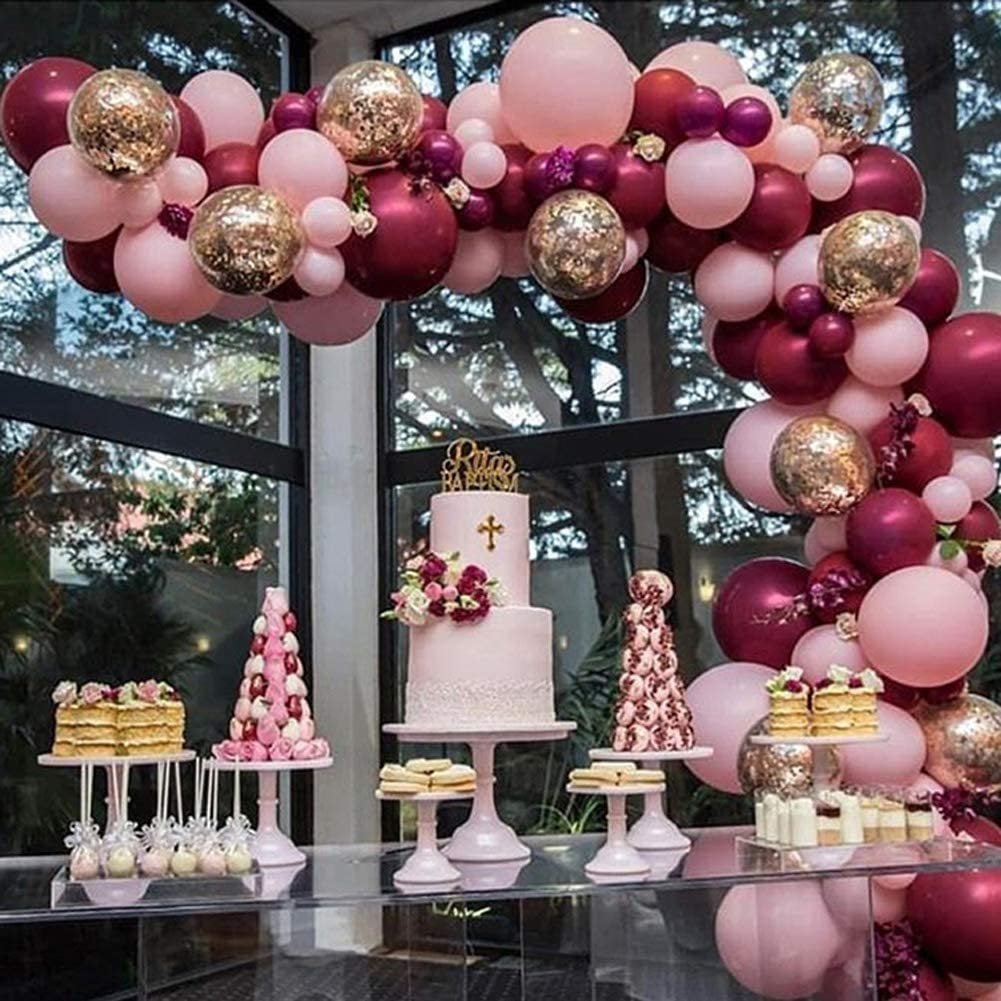 Decorative balloon arch with pink, gold, and red balloons above a dessert table with a cake and various treats.